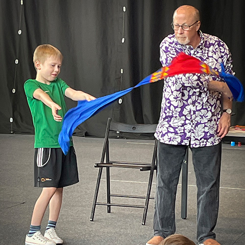 An older man doing a magic trick with a young boy on stage