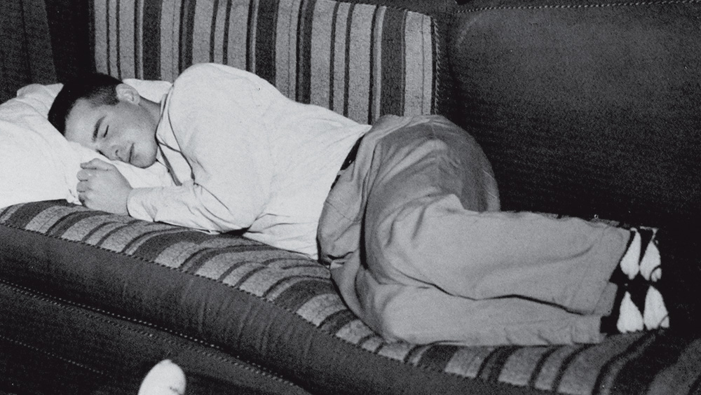 A black and white photo of a young man sleeping on a couch