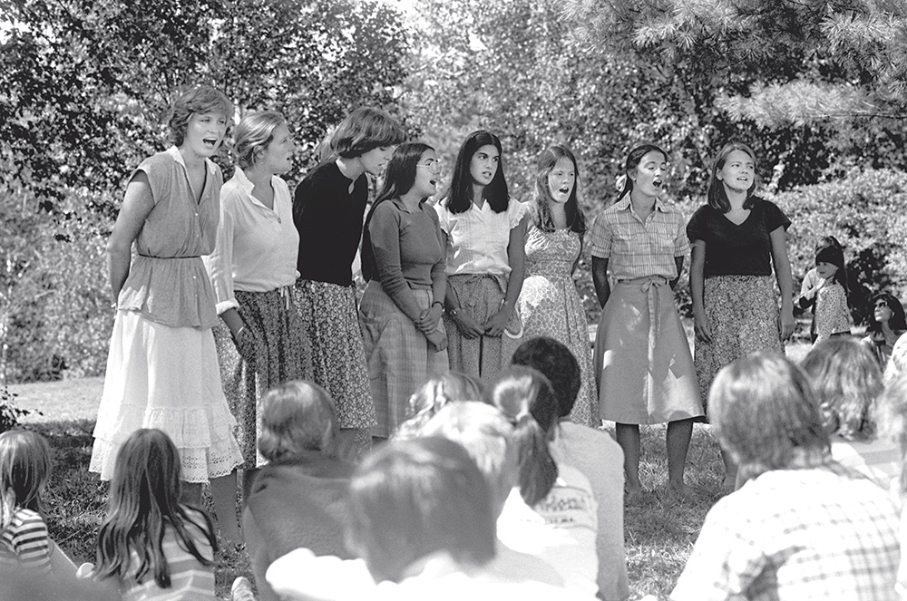 A black and white photo of a line of young woman singing outside