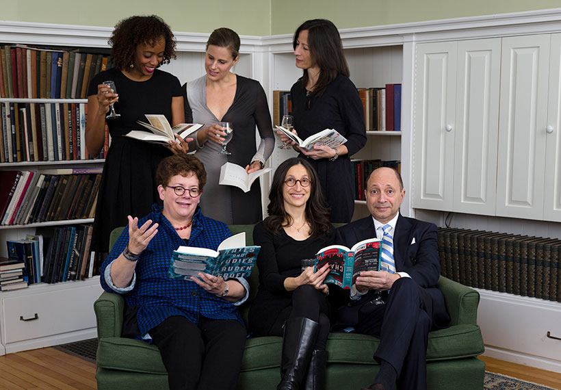 Six people posing together 3 sitting on a couch, 3 standing, all holding books and smiling