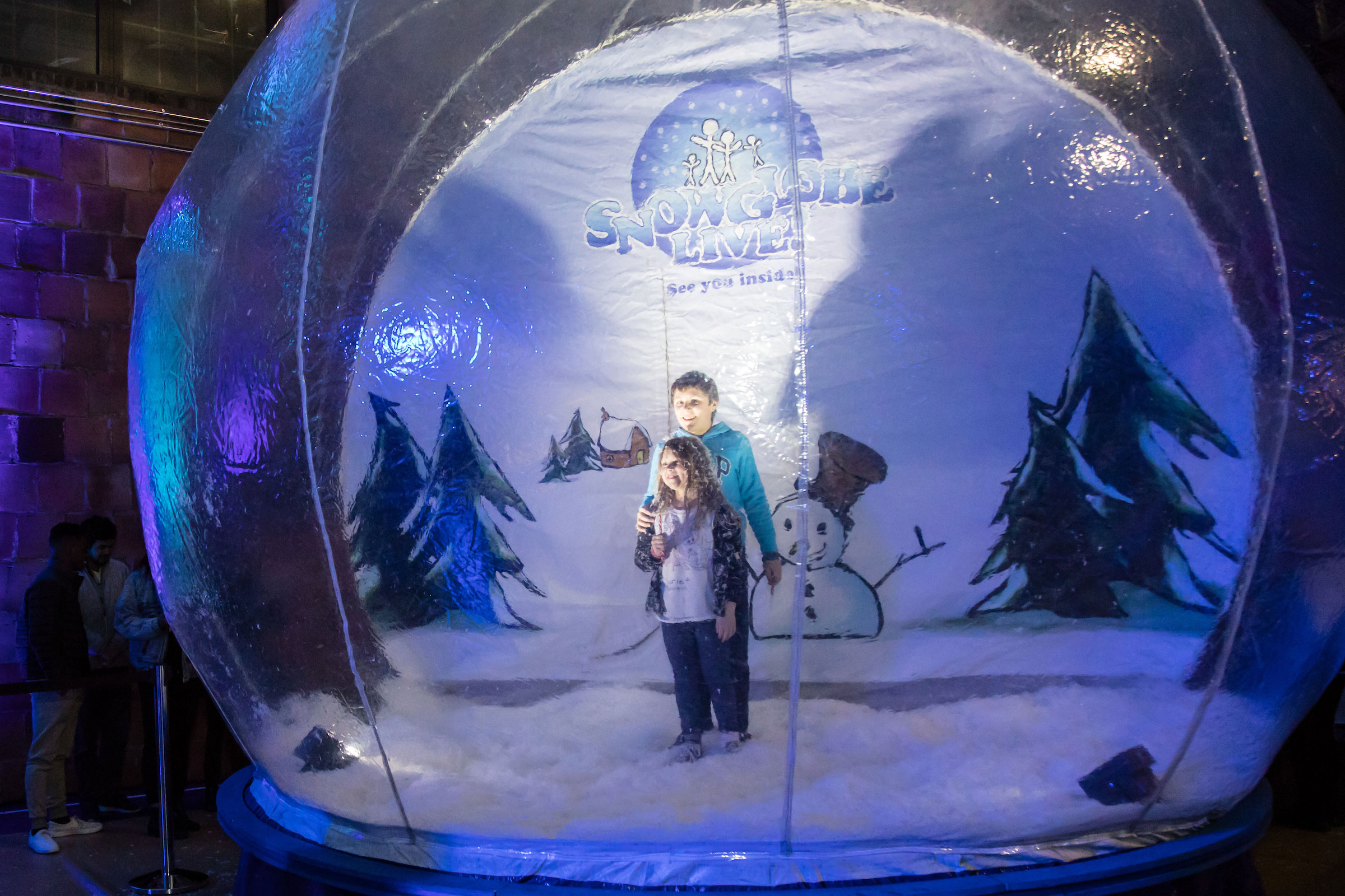 Two children pose inside an inflatable snow globe