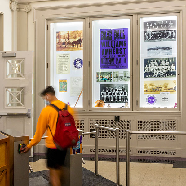 a student in an orange sweatshirt swiping an id card in the gym lobby with the exhibit cases on display