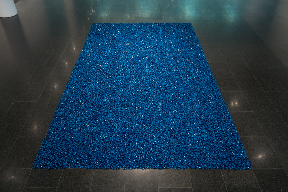 Candies with blue wrappers arranged to form a large rectangle; it glistens against a dark tiled floor.