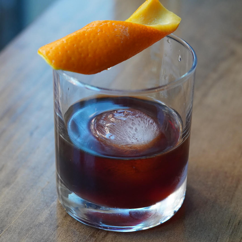 A cocktail with a twist of orange on the rim