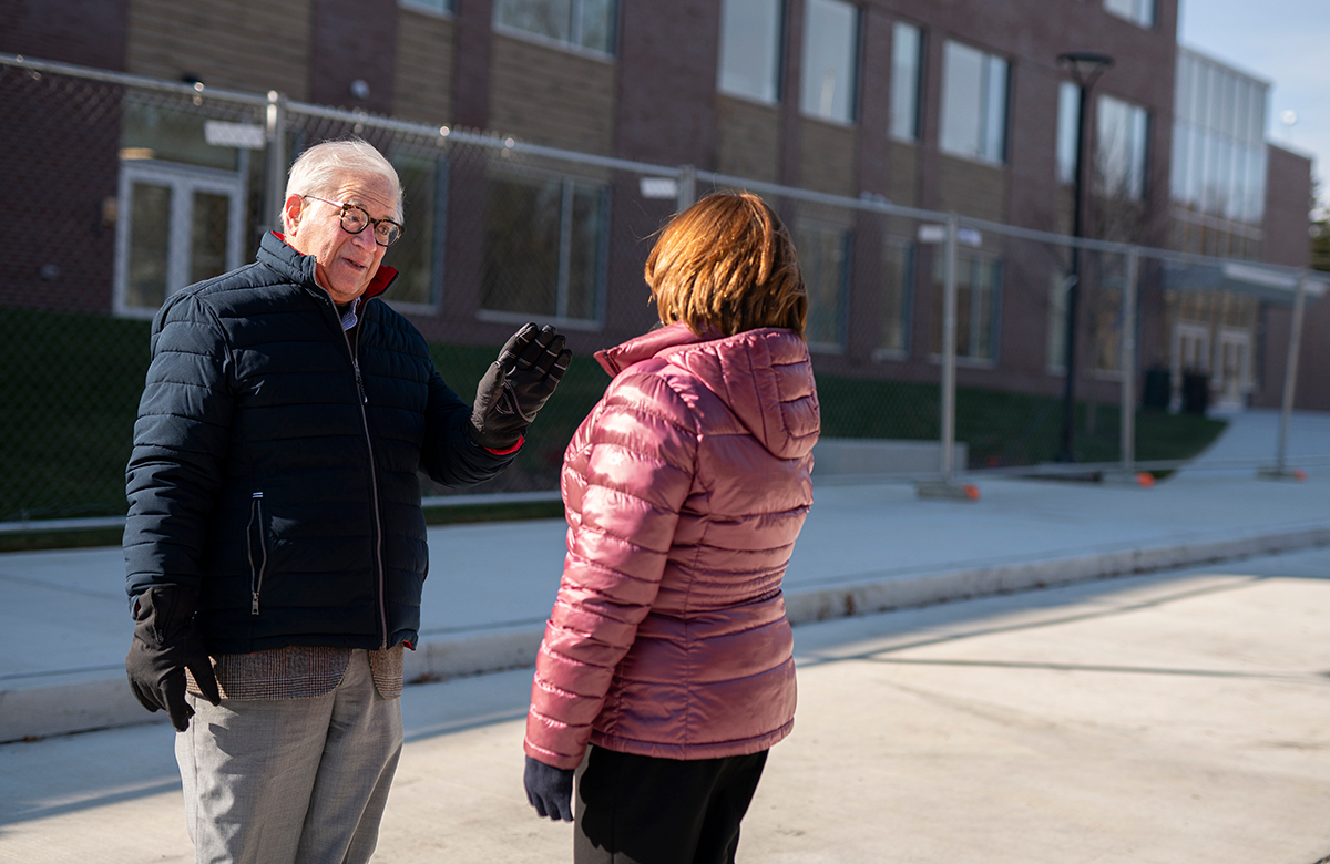 An older man wearing a winter coat talking to a woman on a city street