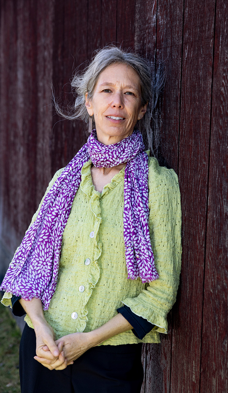 A woman leaning against a wall wearing a green shirt and a purple scarf