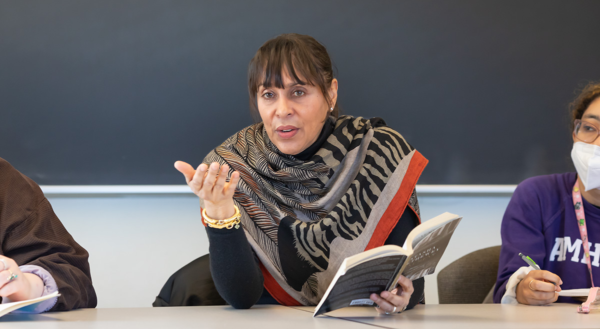 A woman in a colorful shawl holding a book and speaking in a classroom