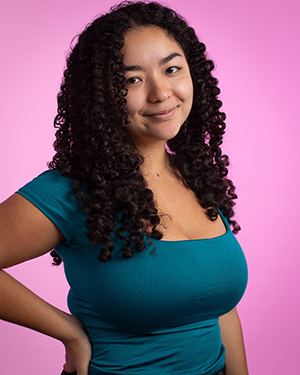 A young woman with long curly hair and a green shirt against a pink background