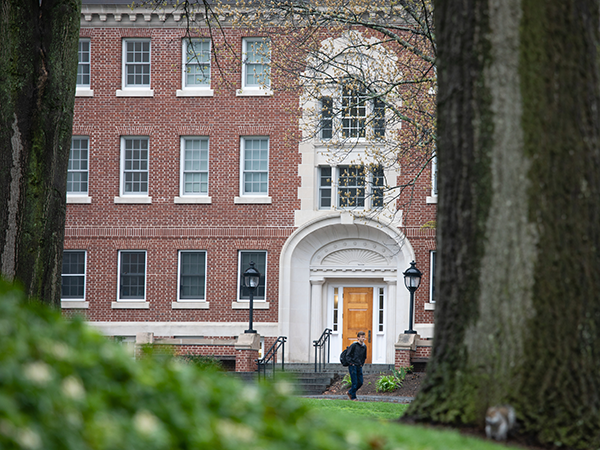 A student walking in front of a dorm from behind trees