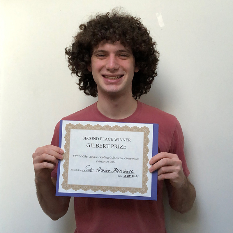 A young man with curly hair holding a certificate and smiling