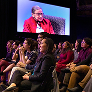 A group of students with a large video screen showing Ruth Bader Ginsberg