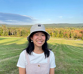 A woman in a white t-shirt and a sunhat standing on an open sunny field.