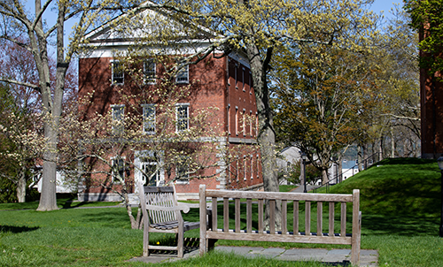 A three-story brick building with benches and spring trees in bloom
