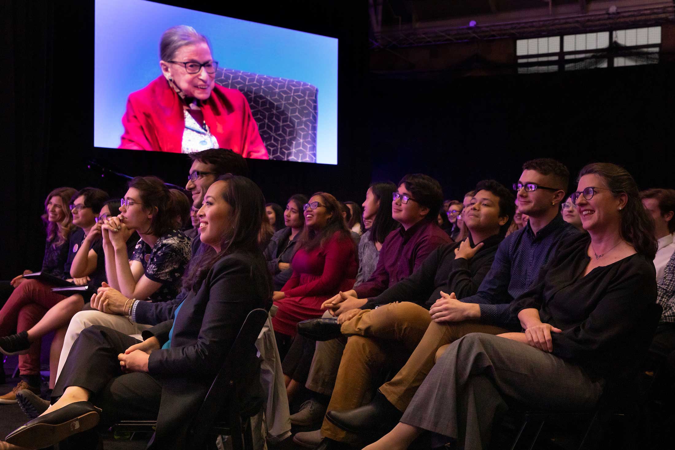 The audience listening to Justice Ginsburg who is shown on the large display screen in the venue