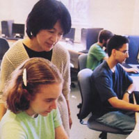 A teacher learning over a student on a computer instructing her