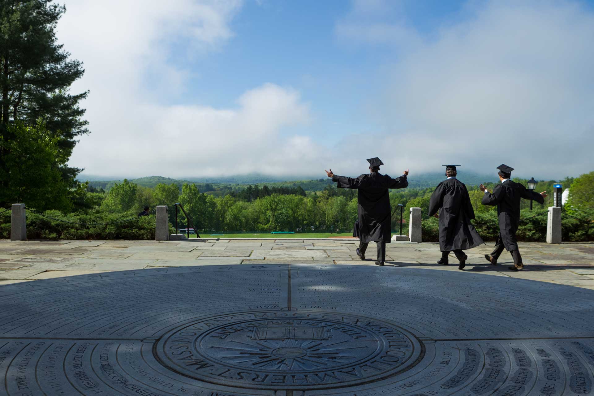 three graduates walk toward the mountain range and blue sky