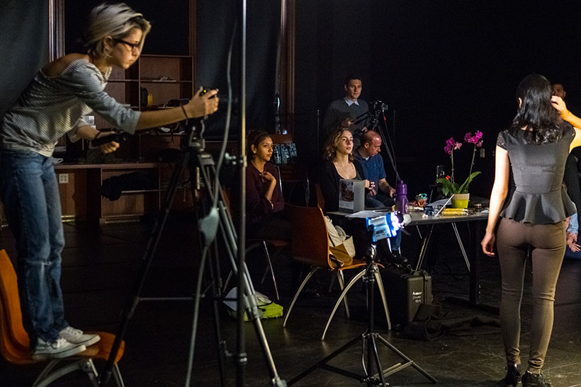 a woman films actors performing on a stage set