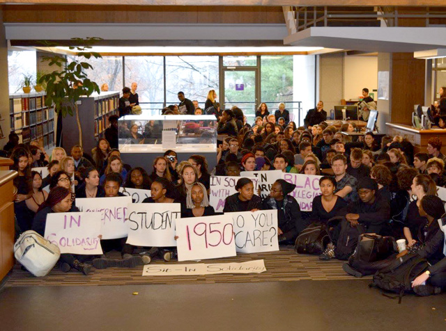 students sitting on the floor of the Frost Library lobby holding protest signs saying 1950 and Do you care?