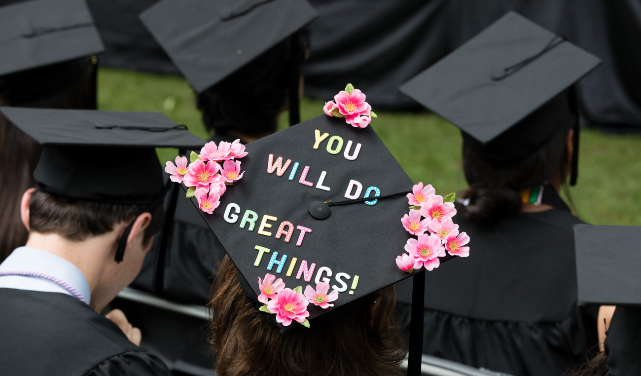a graduate wears a cap embellished with flowers and the words You will do great things