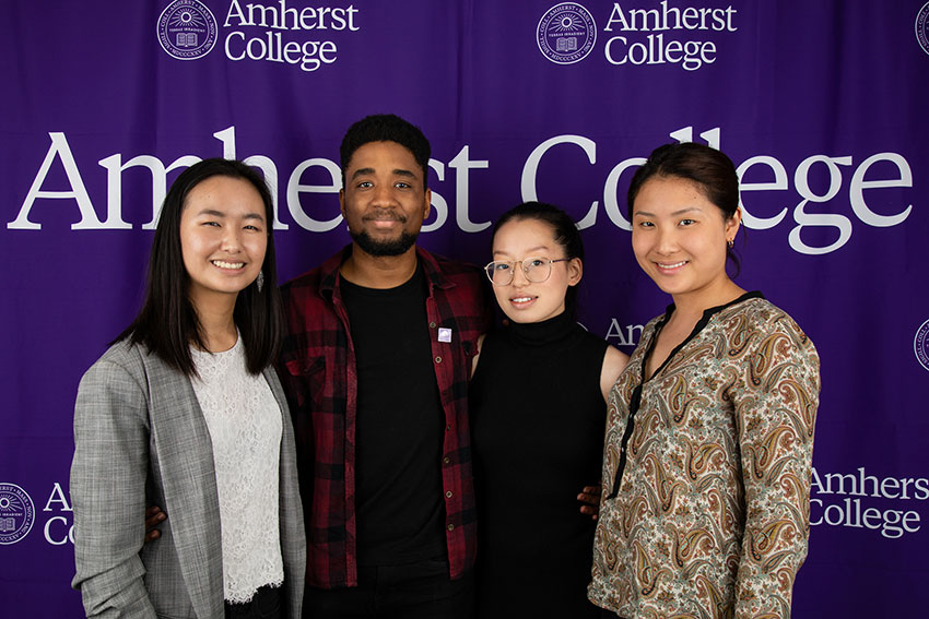 Four students posing in front of an Amherst College banner