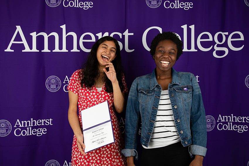 Two smiling students posing in front of an Amherst College banner