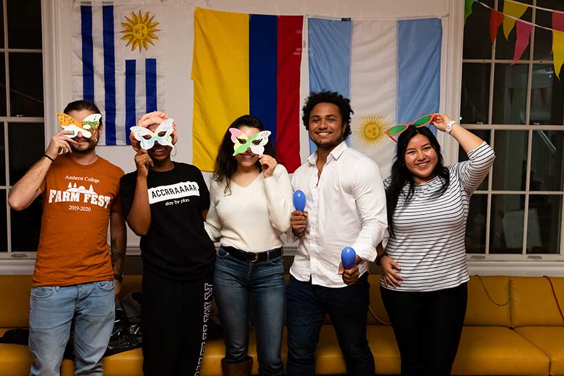 Five people pose for a photo infront of international flags, three of them are holding masks to their faces