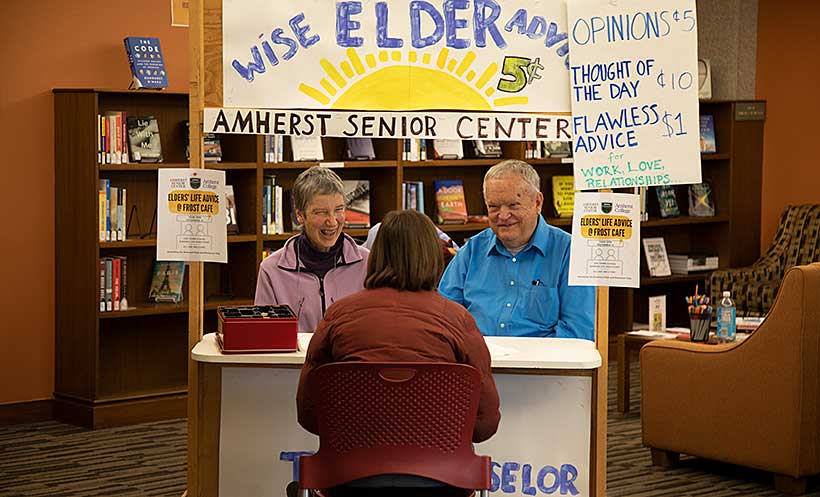 Two people sit before an information booth titles Wise Elders Advice, Amherst Senior Center