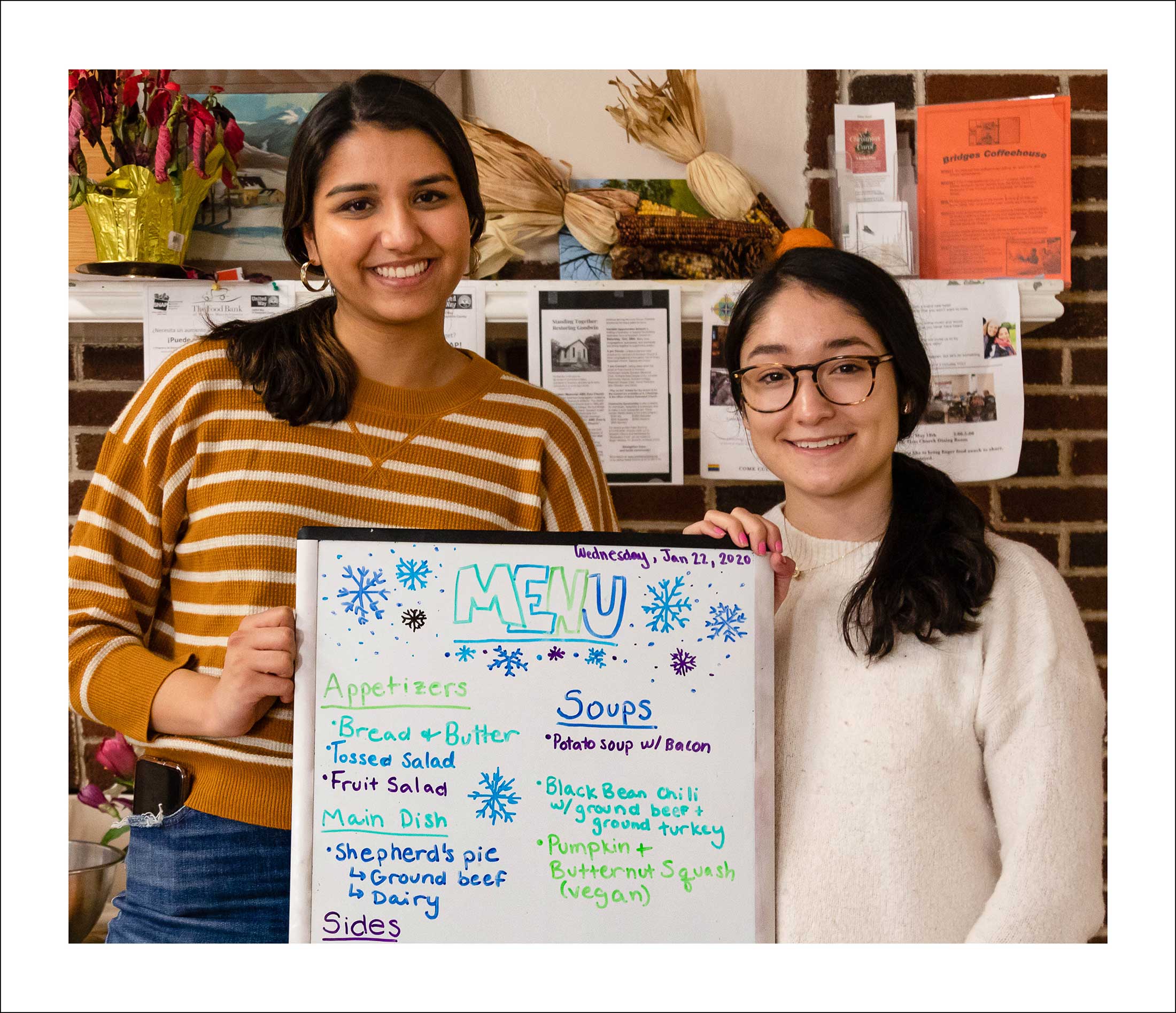 Two women holding a white board covered with writing