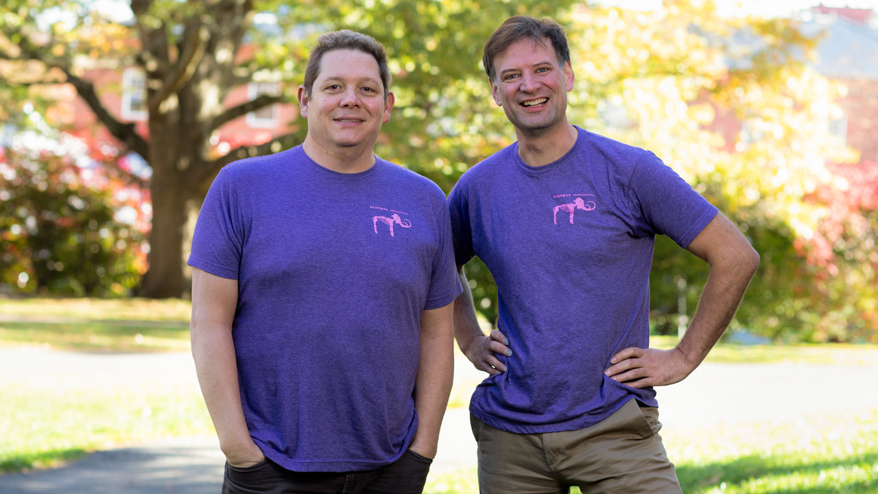 two professors wear the same t-shirt with a mammoth skeleton on the front