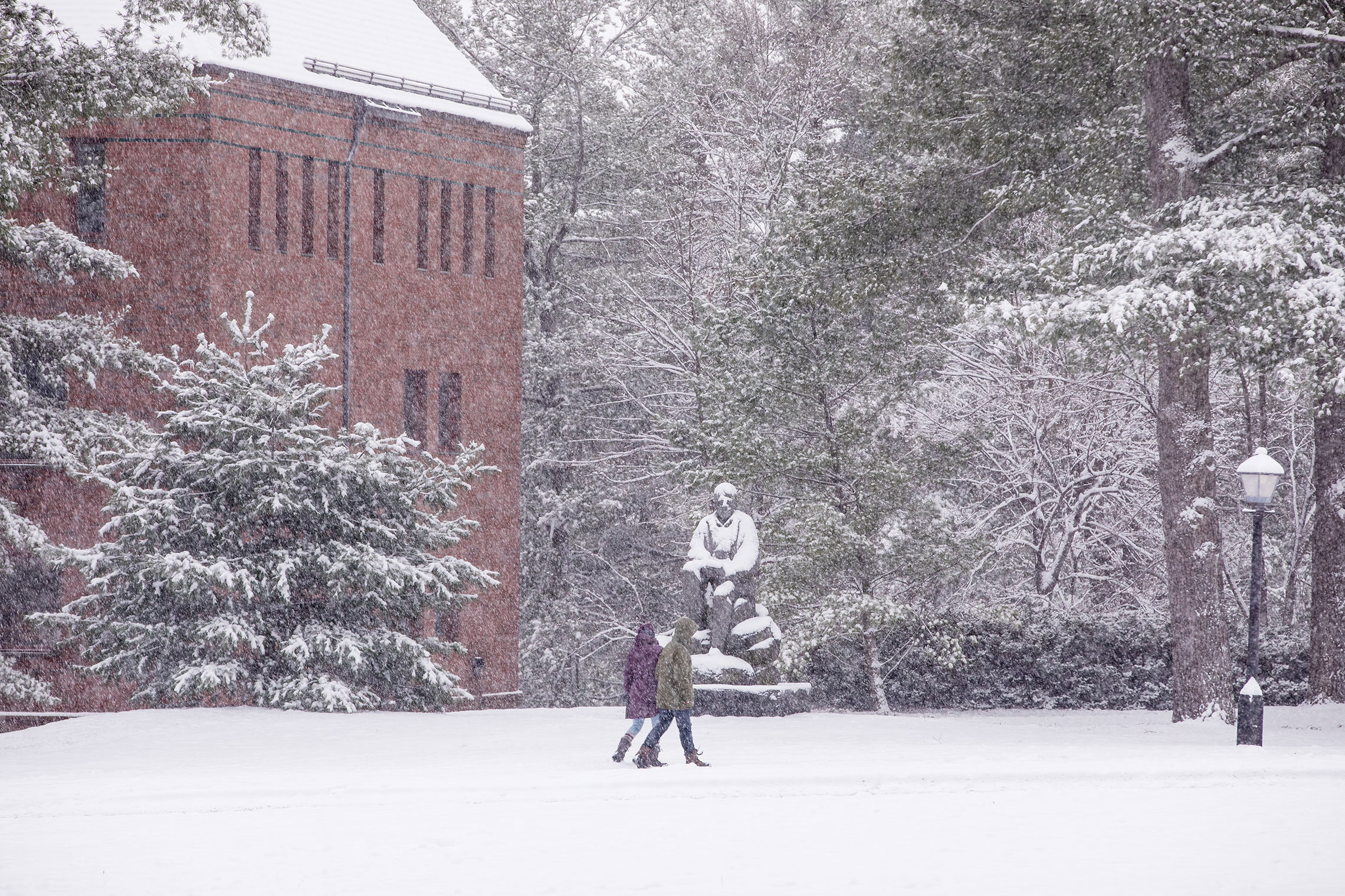 Students passing by a statue of Robert Frost on a snowy day.