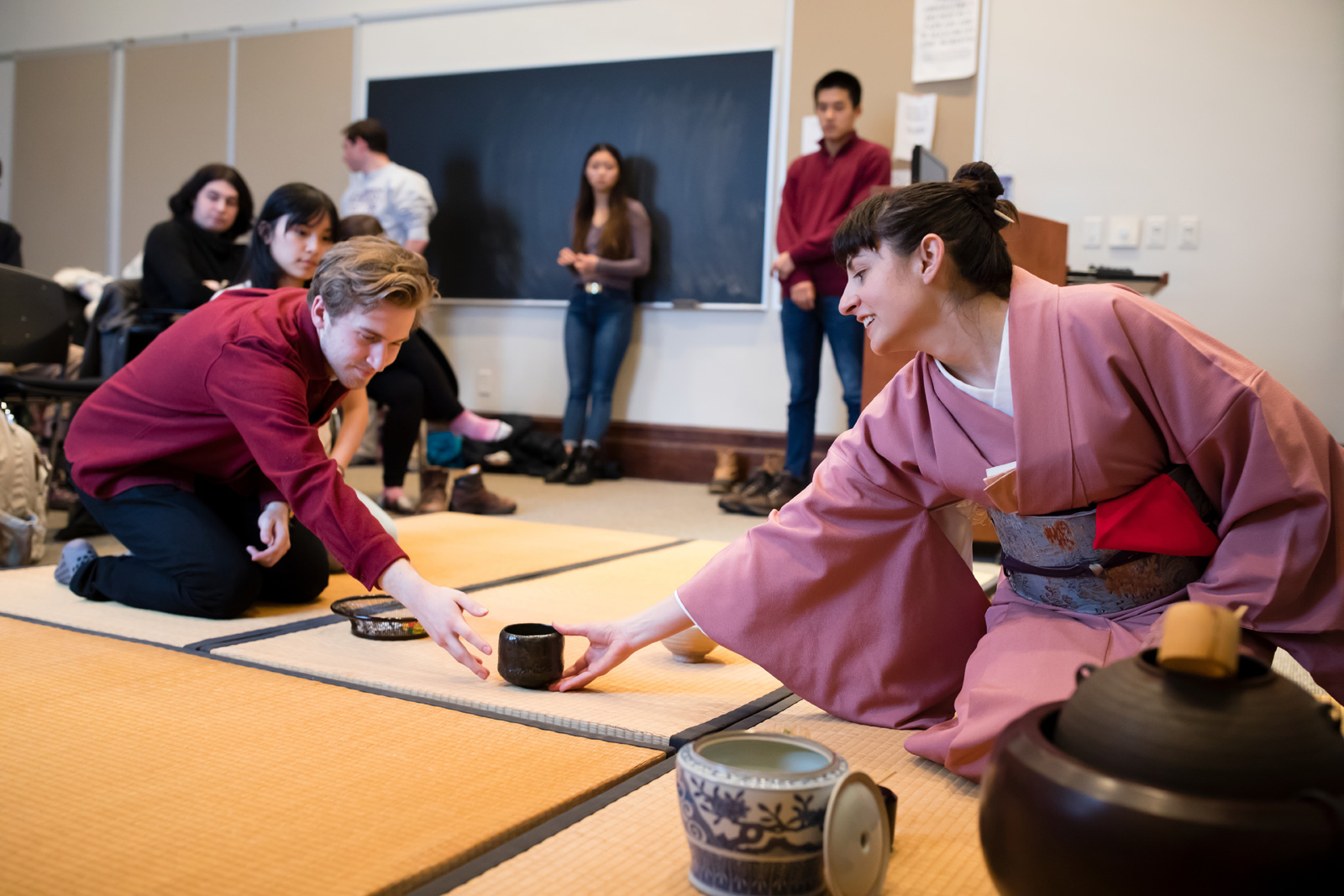 The ceremony leader, dressed in a kimono, hands a cup of tea to a student