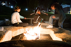 Three students sitting in front of a fire pit at night