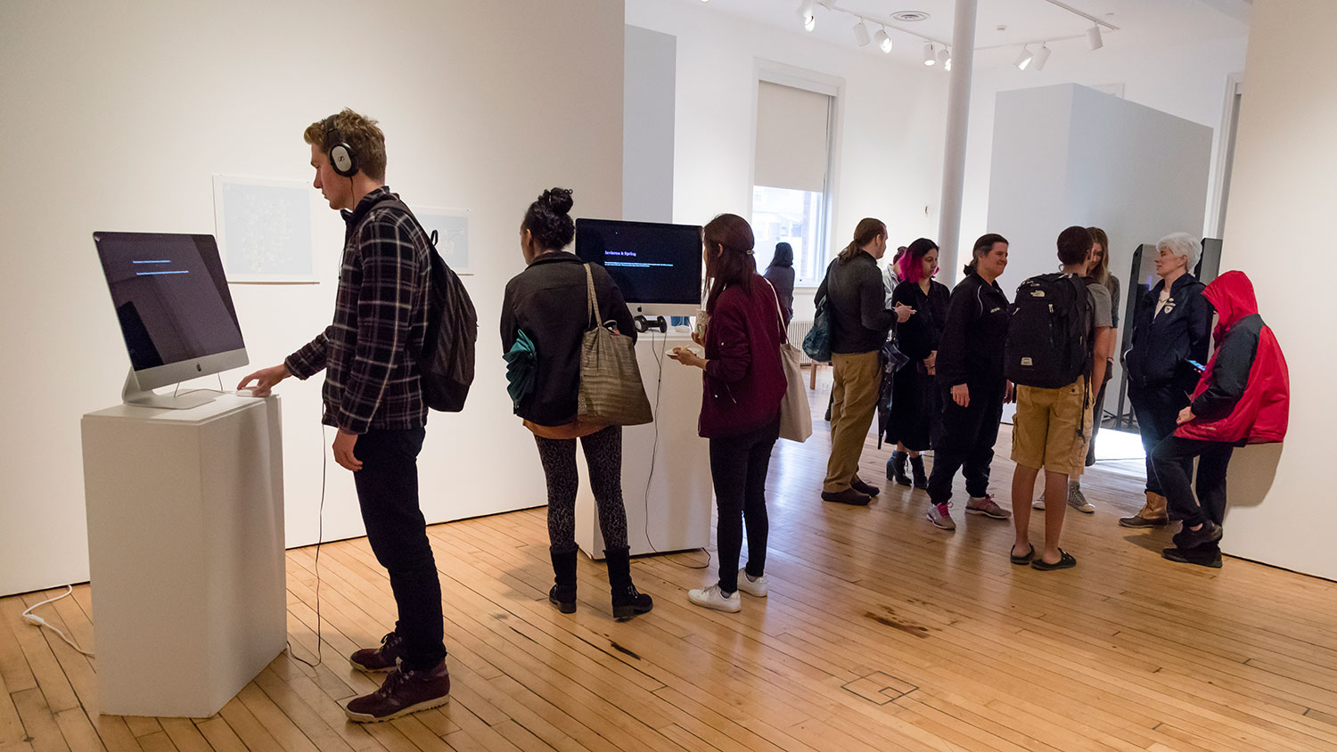 Gallery goers mingle around pedestals with TVs set up on top