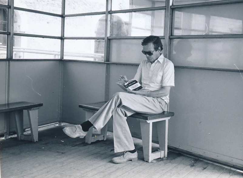 A man in sunglasses sitting on a bench reading a guidebook