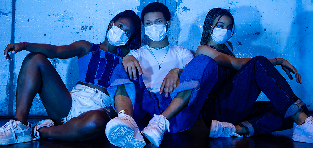 Three people sitting in a room filled with blue light wearing face masks