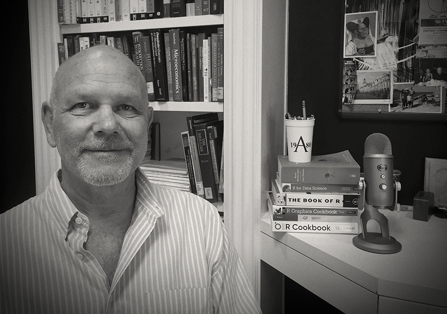 A black and white photo of a bearded man in a study in front of bookshelves