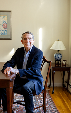 A photo of an older man in a suit sitting in a living room