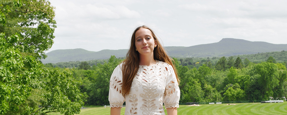 A young woman in a white dress in front of the Holyoke Range