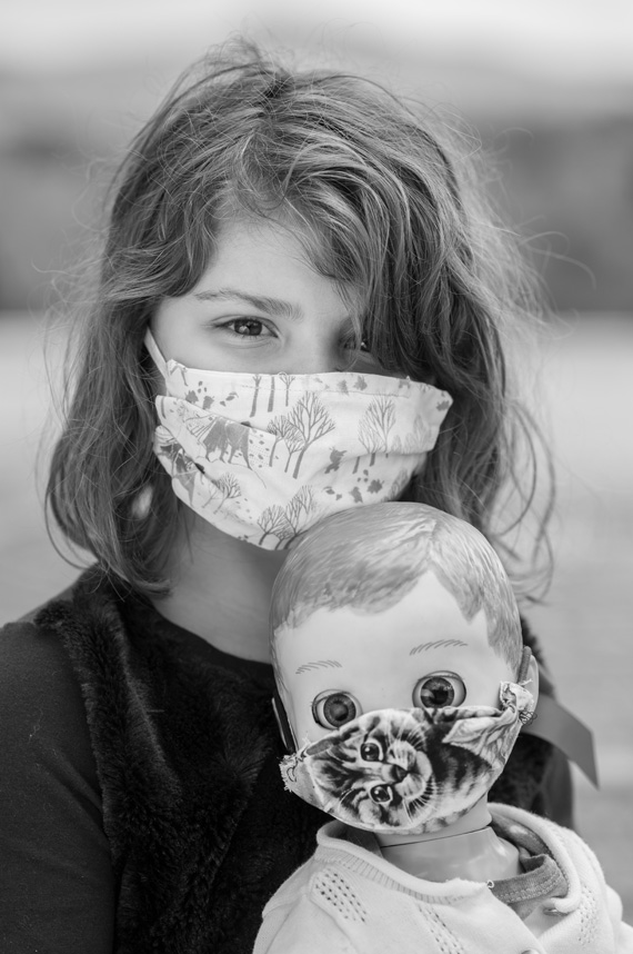 young Avelynn Augustin wears a mask while holding a doll wearing a mask