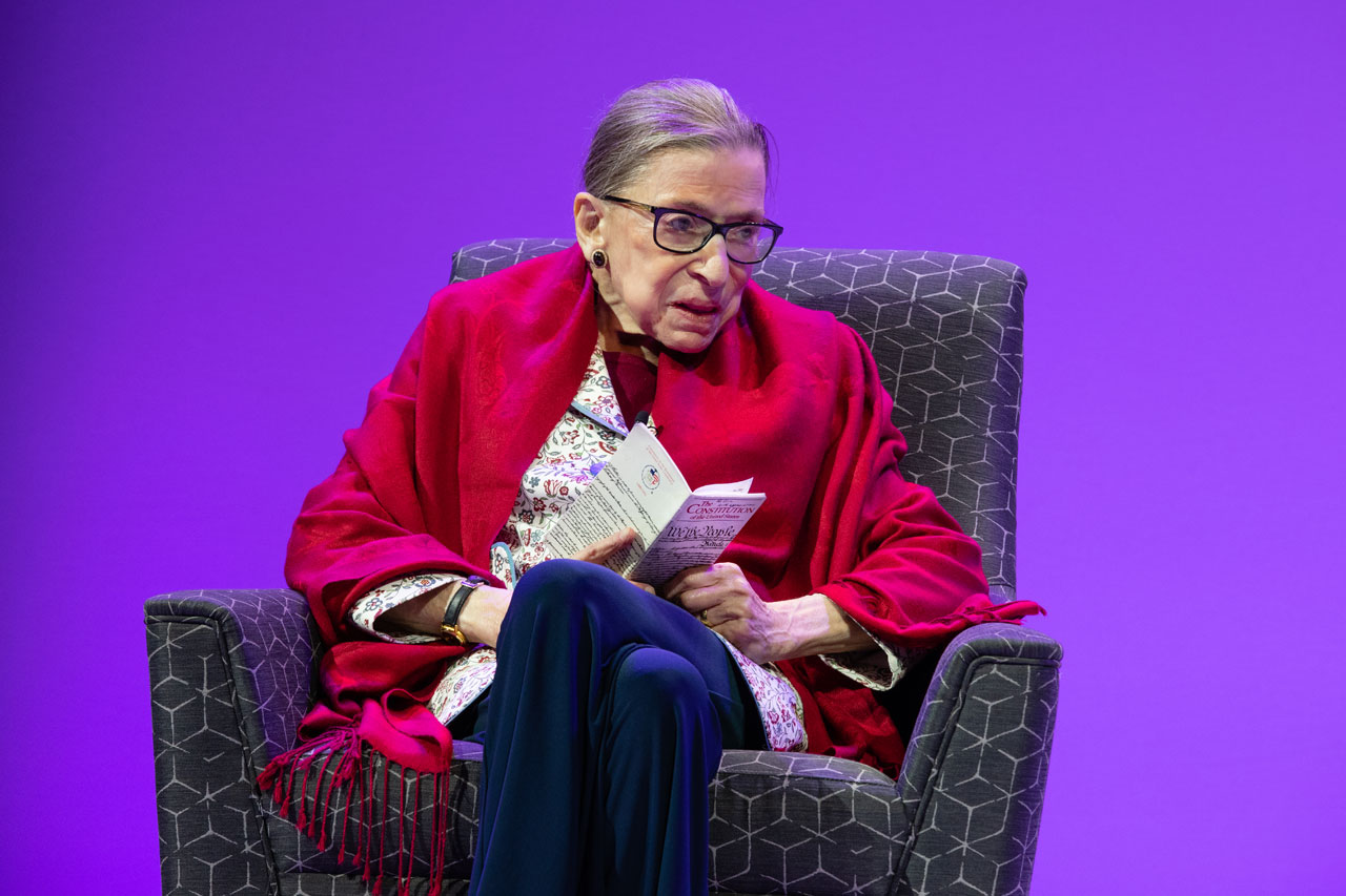 Ruth Bader Ginsburg sitting in front of purple background