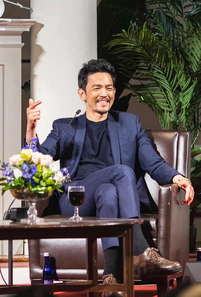 A photo of an Asian man in a blue suit smiling on stage