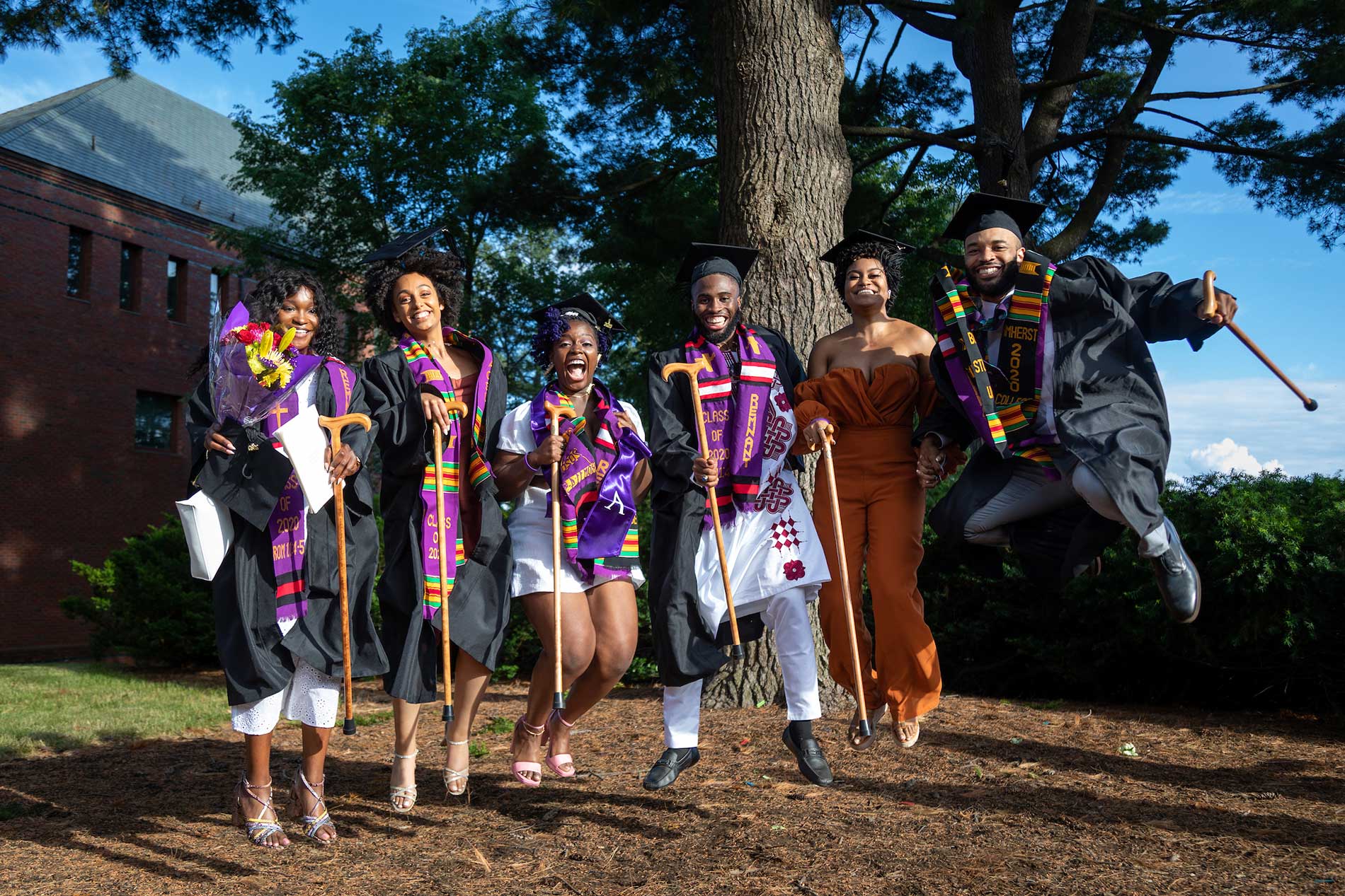 A group of graduates wearing regalia jump in unison.