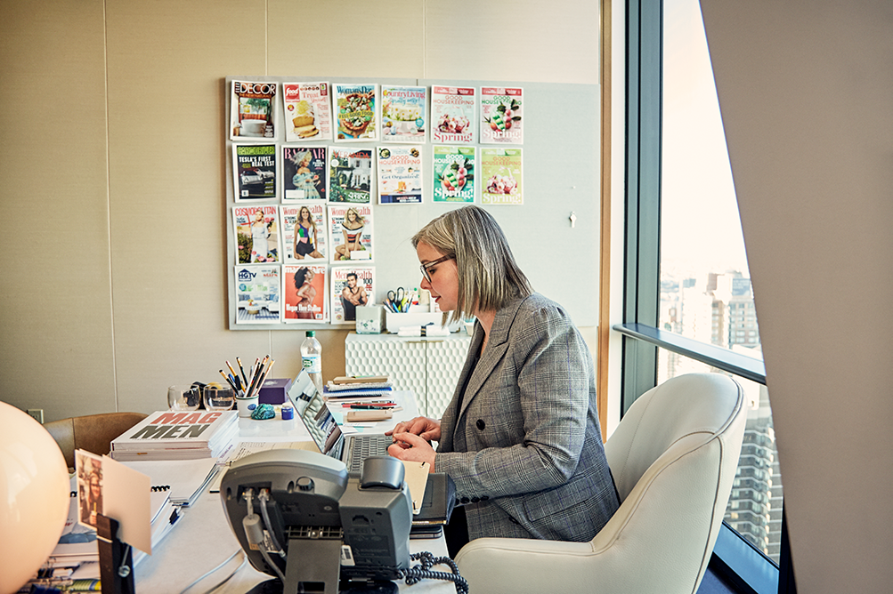 A woman at a desk kin a office with magazine covers on the wall.
