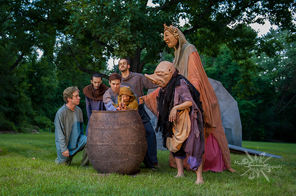 Actors and puppets gathered around a cauldron