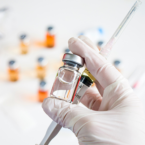 A hand holding a vaccine bottle and needle