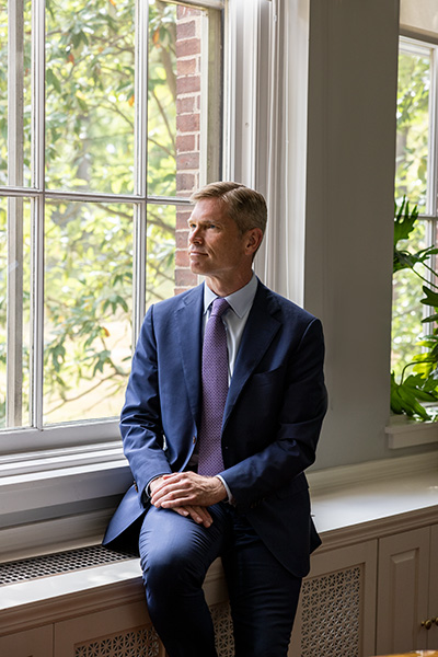 A man in a blue suit sitting on a window sill looking out the window
