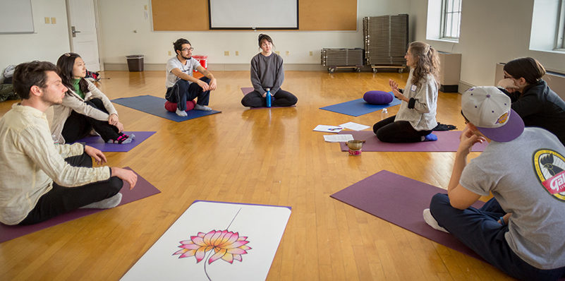 A group of students sitting in a semi-circle on yoga mats