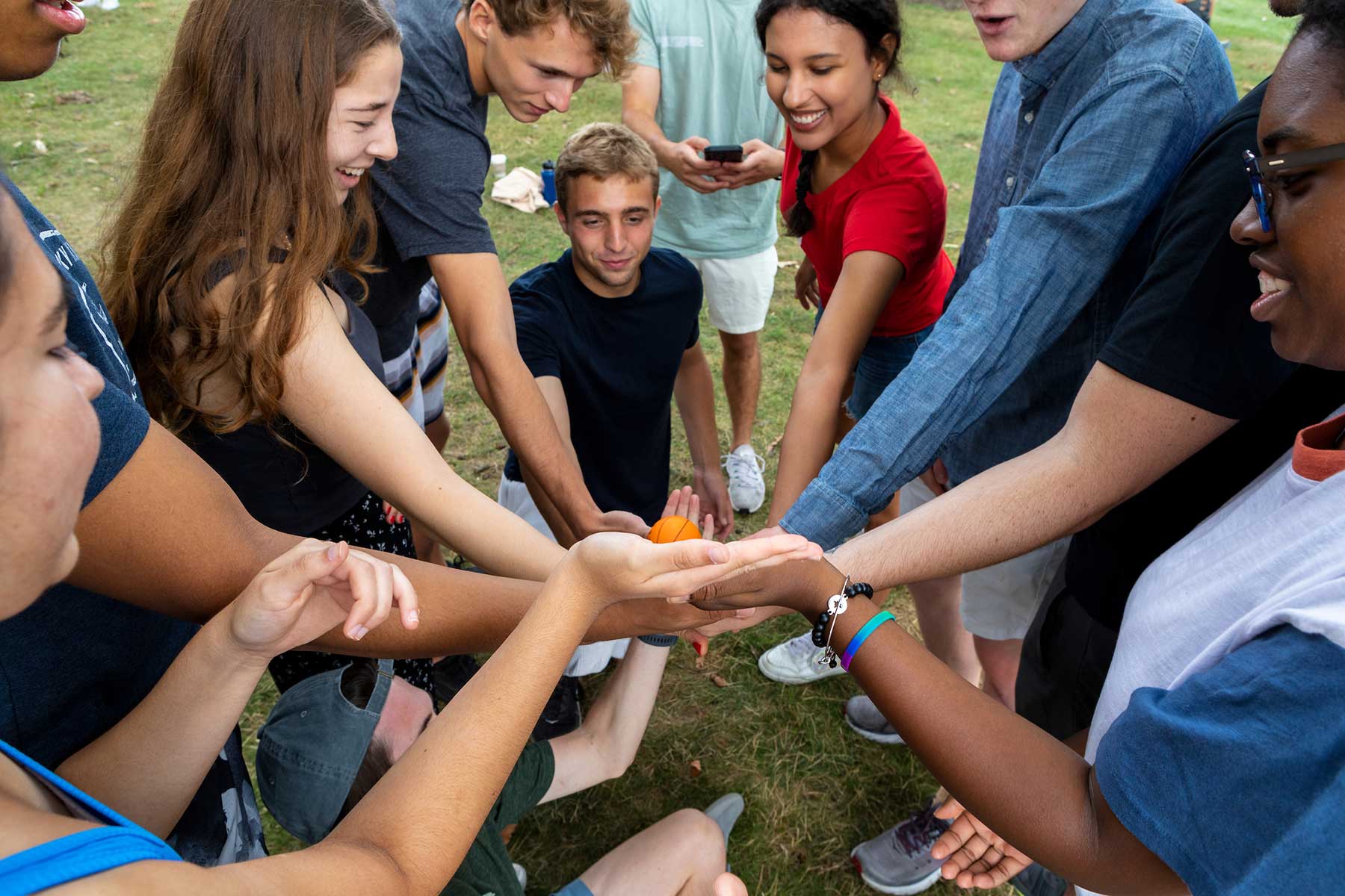 A group of college students stand in a circle, stacking their hands in the center.