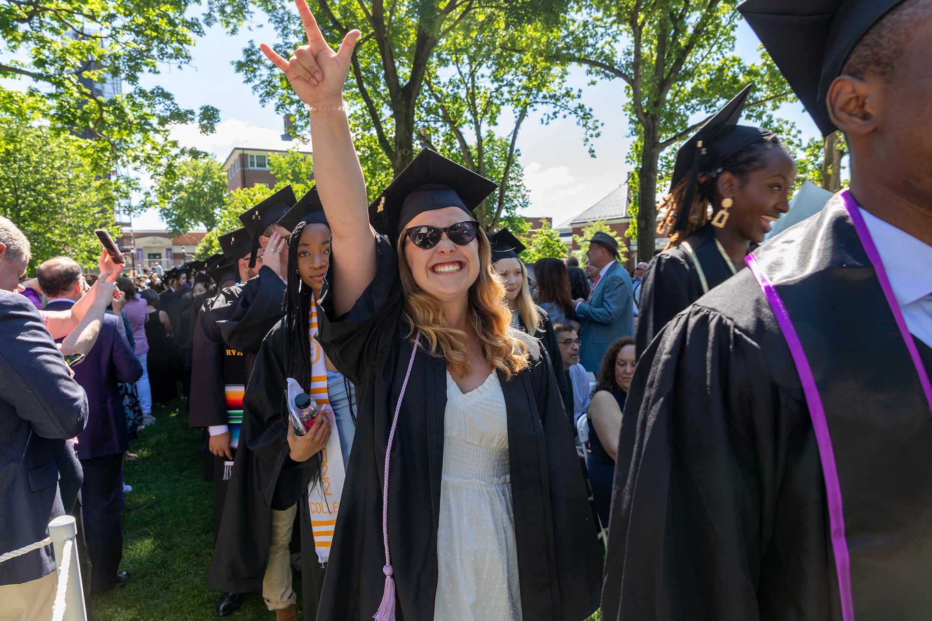 A female student, walking in line with other robed graduates, raises her fist in celebration.