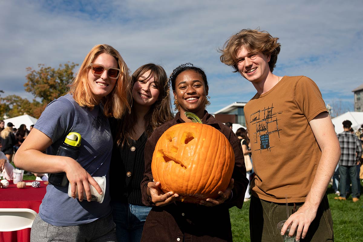 Four students pose with a carved pumpkin.